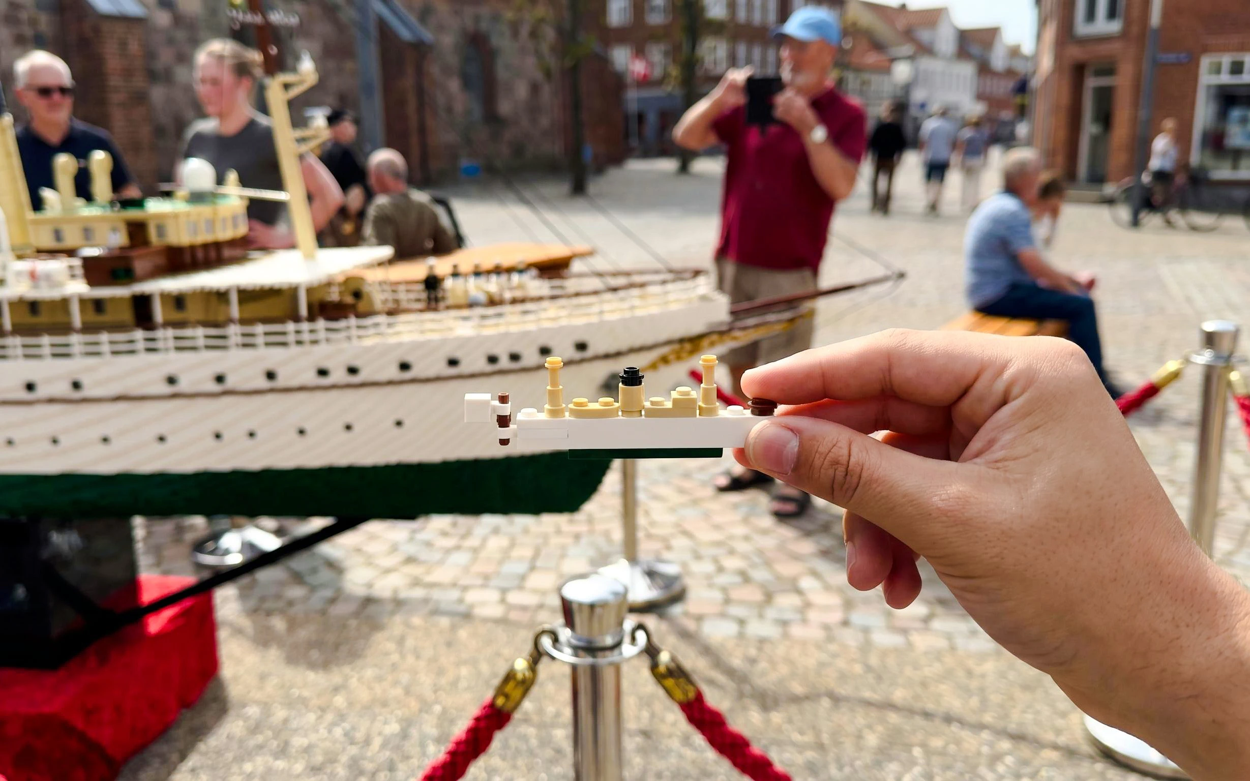 Hand holding LEGO piece in front of a LEGO ship model at LEGOLAND Miniland.