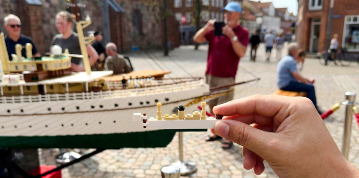 Hand holding LEGO piece in front of a LEGO ship model at LEGOLAND Miniland.