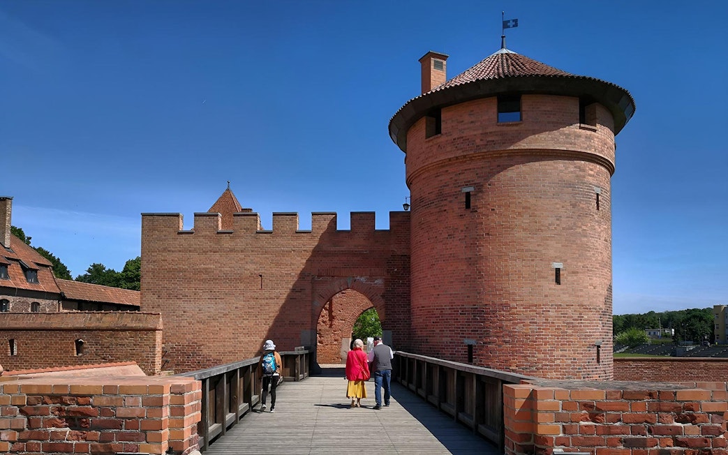 Visitors walking on a bridge towards Malbork Castle tower during a tour from Gdańsk.
