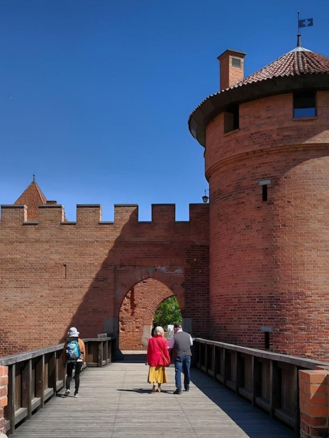 Visitors walking on a bridge towards Malbork Castle tower during a tour from Gdańsk.