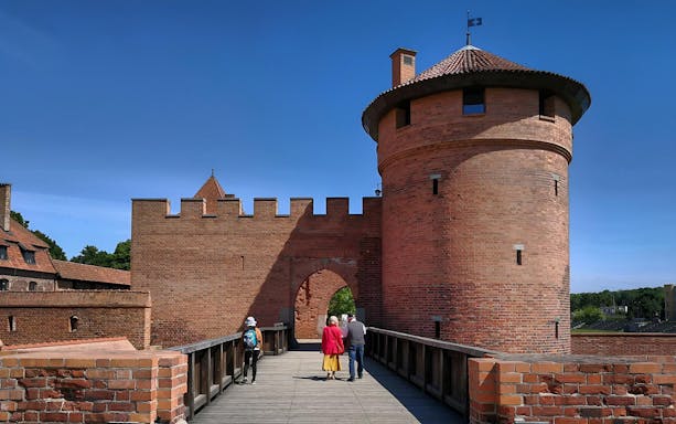 Visitors walking on a bridge towards Malbork Castle in Poland.