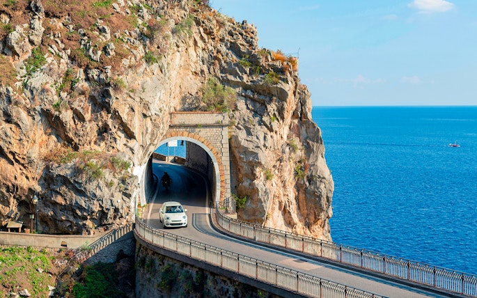 Car driving through a coastal tunnel on the Amalfi Coast with sea views.