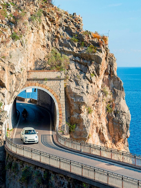 Car driving through a coastal tunnel on the Amalfi Coast with sea views.