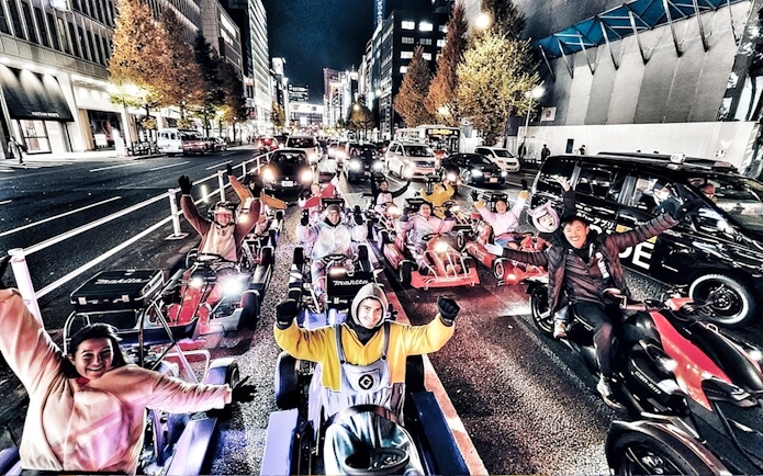 Group in costumes driving go-karts on a city street at night.