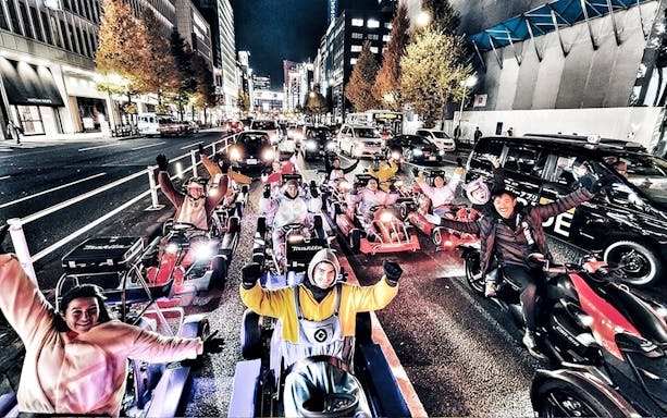 Group in costumes driving go-karts on a city street at night.