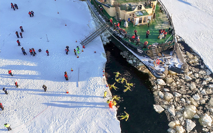 Icebreaker Sampo cruise passengers in thermal suits floating in icy water near Kemi, Finland.