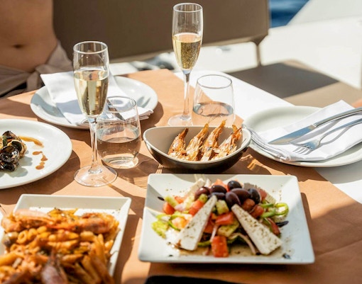 Santorini luxury catamaran cruise meal with seafood, salad, and wine on a table overlooking the Aegean Sea.