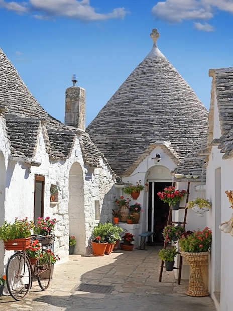 Trulli houses with conical roofs in Apulia, Italy, surrounded by potted plants and a bicycle.