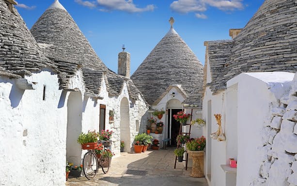 Trulli houses with conical roofs in Apulia, Italy, surrounded by potted plants and a bicycle.