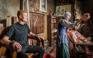 Man in a torture chamber with medieval tools at London Dungeon.