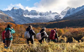 Hikers trekking towards Esmeralda Lake with snow-capped mountains in the background.