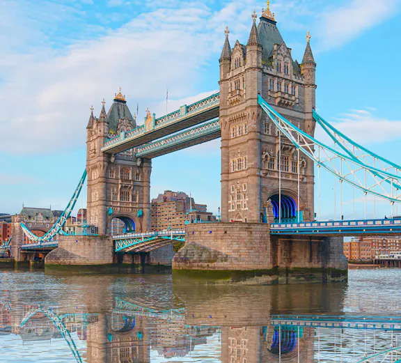 Tower Bridge spanning the Thames River in London, reflecting in the water.