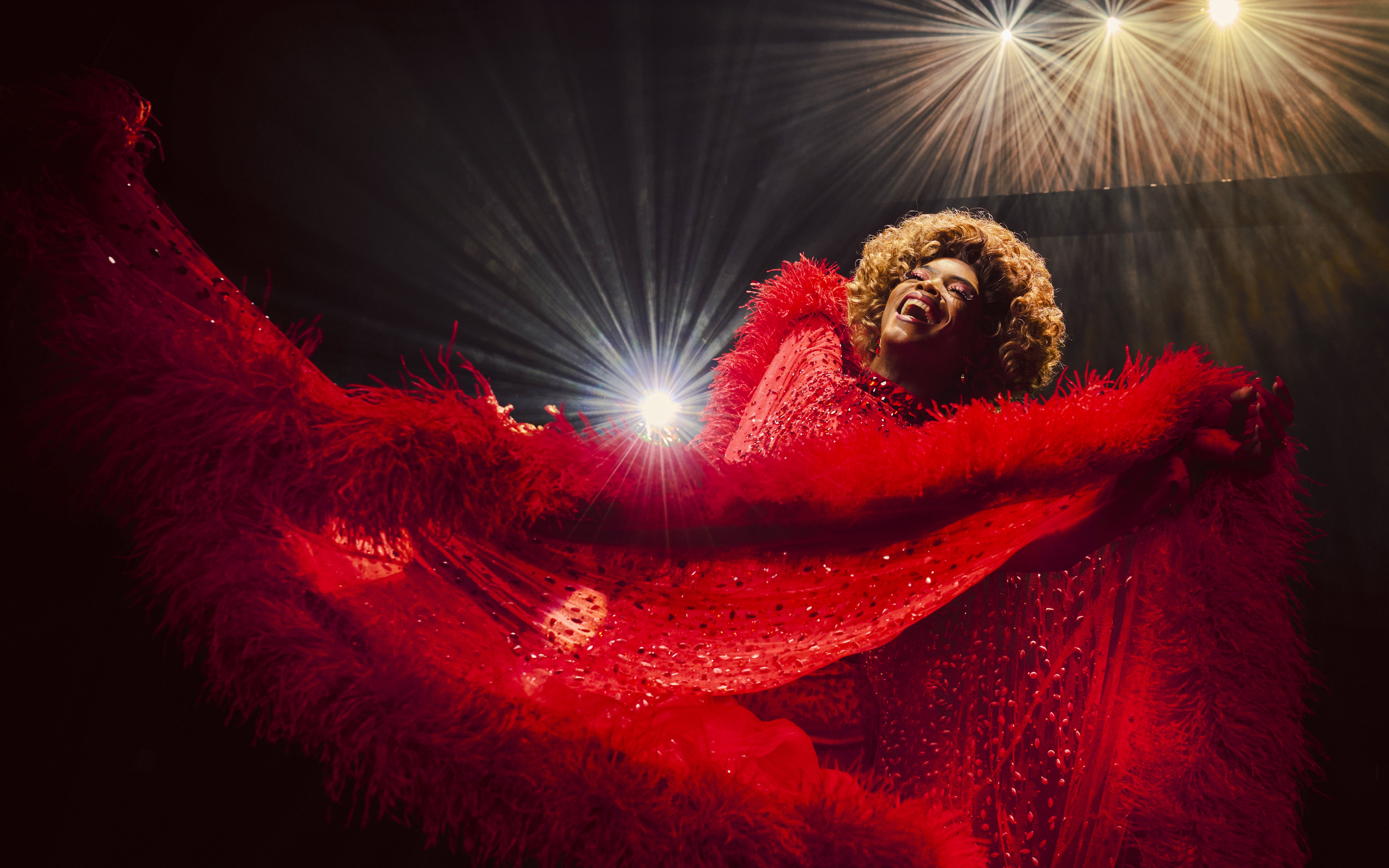 Performer in vibrant red costume on stage during Kinky Boots production.