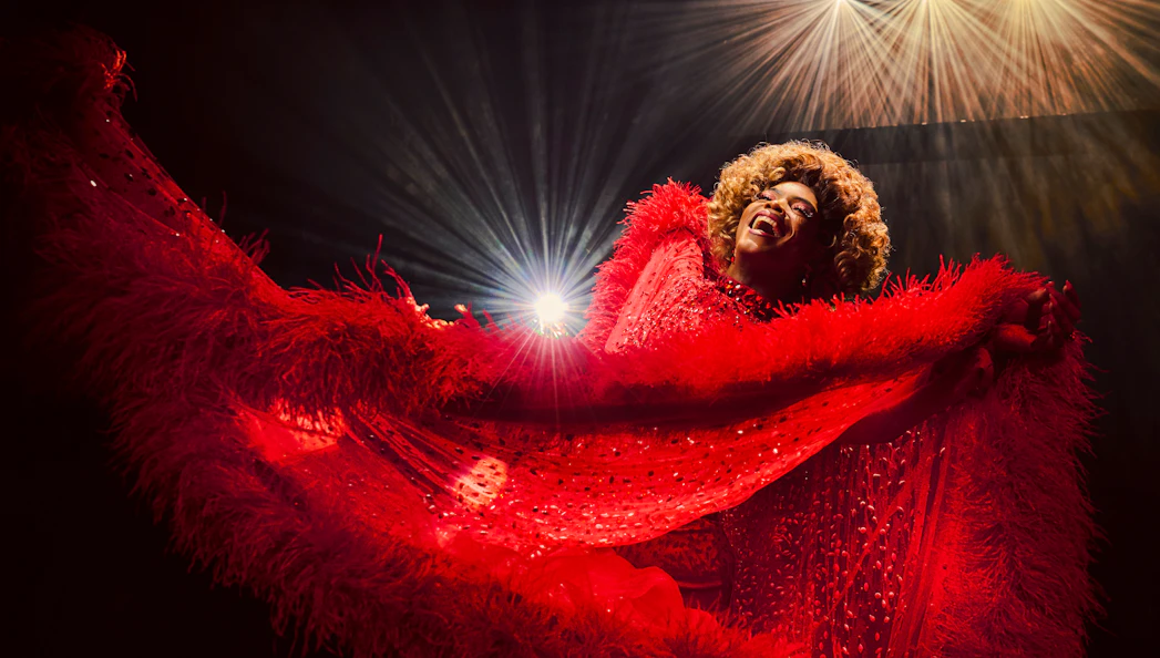 Performer in vibrant red costume on stage during Kinky Boots production.