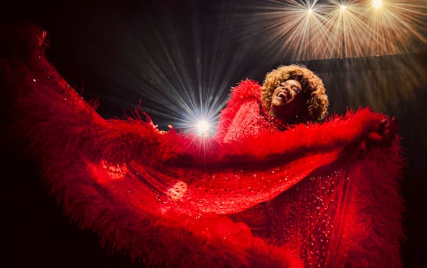 Performer in vibrant red costume on stage during Kinky Boots production.