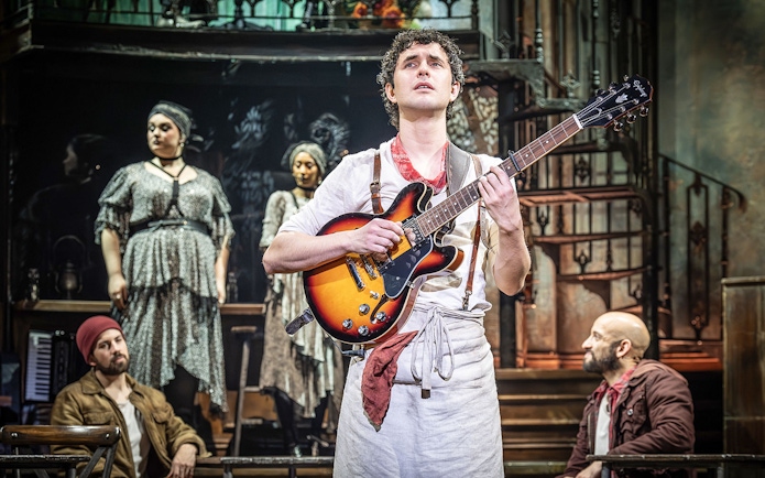 Performer playing guitar on stage during Hadestown musical.