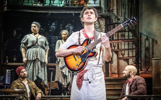 Performer playing guitar on stage during Hadestown musical.