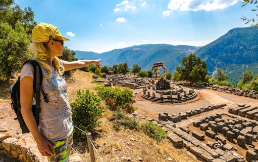 Guests exploring Delphi archaeological site with a guide pointing at ruins.