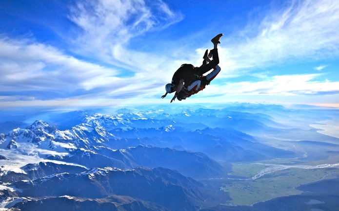Skydiver over Franz Josef Glacier, New Zealand, with mountain views.