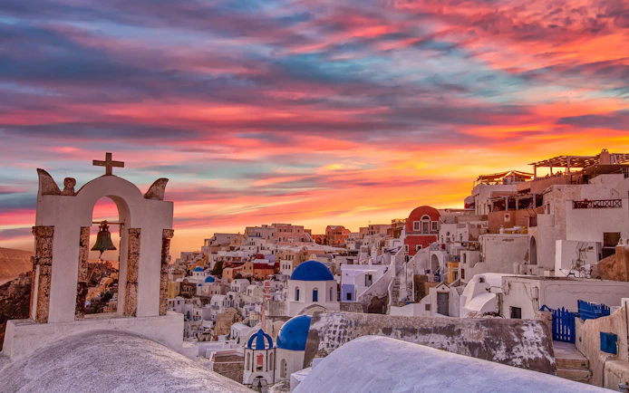 Oia village at sunset with white buildings and blue domes in Santorini, Greece.