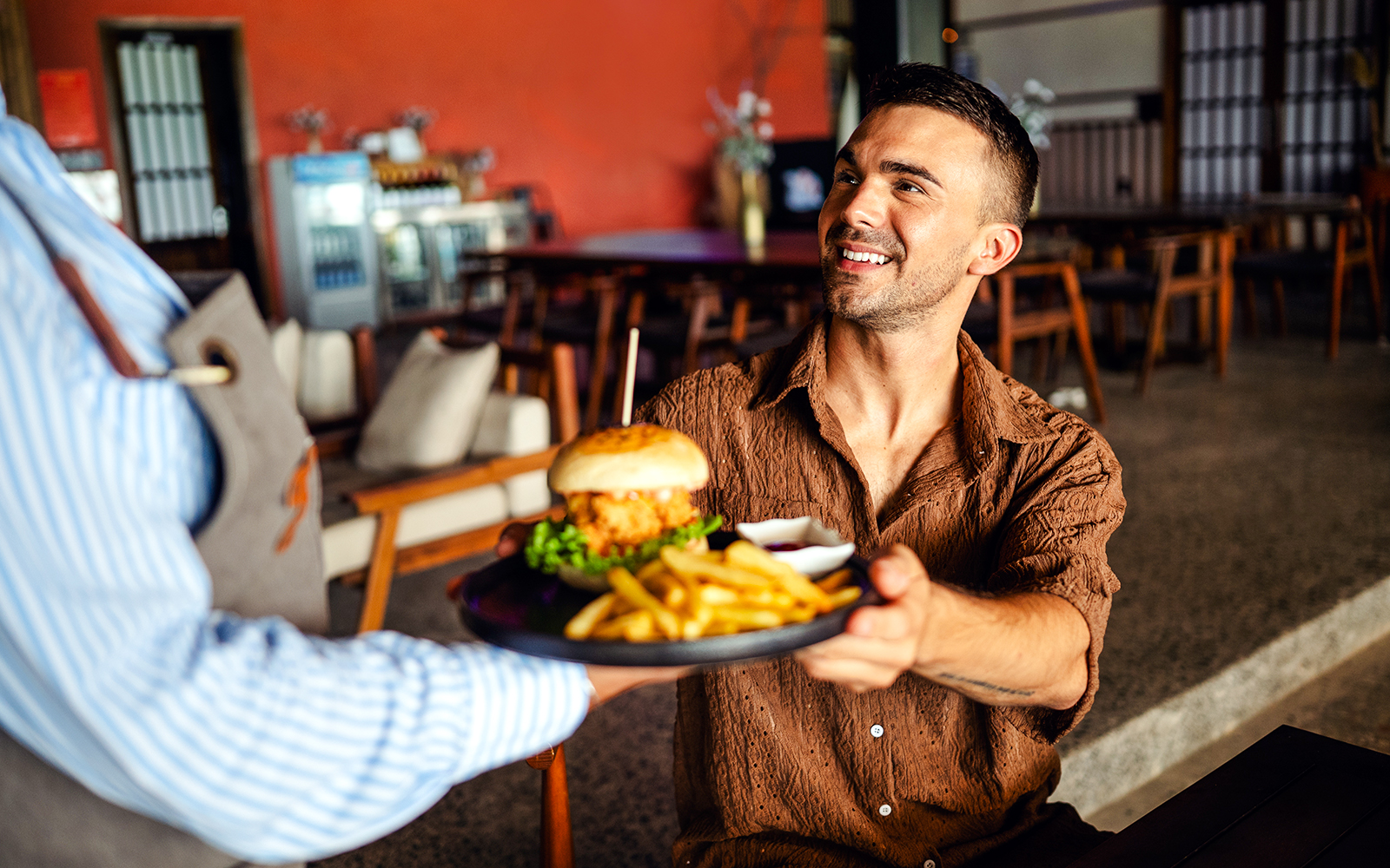 Waitress serves a burger and fries to a smiling customer in a restaurant.