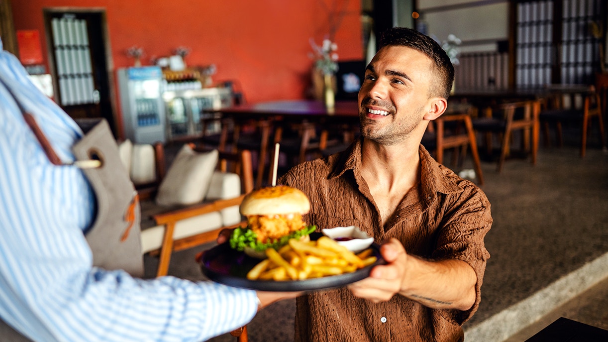 Waitress serves a burger and fries to a smiling customer in a restaurant.