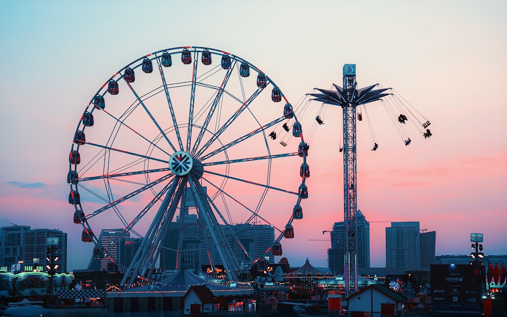 Ferris wheel and swing ride at Lusail Winter Wonderland at sunset.