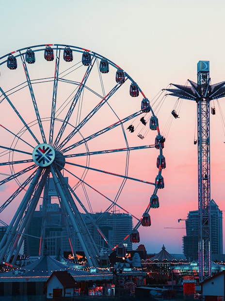 Ferris wheel and swing ride at Lusail Winter Wonderland at sunset.
