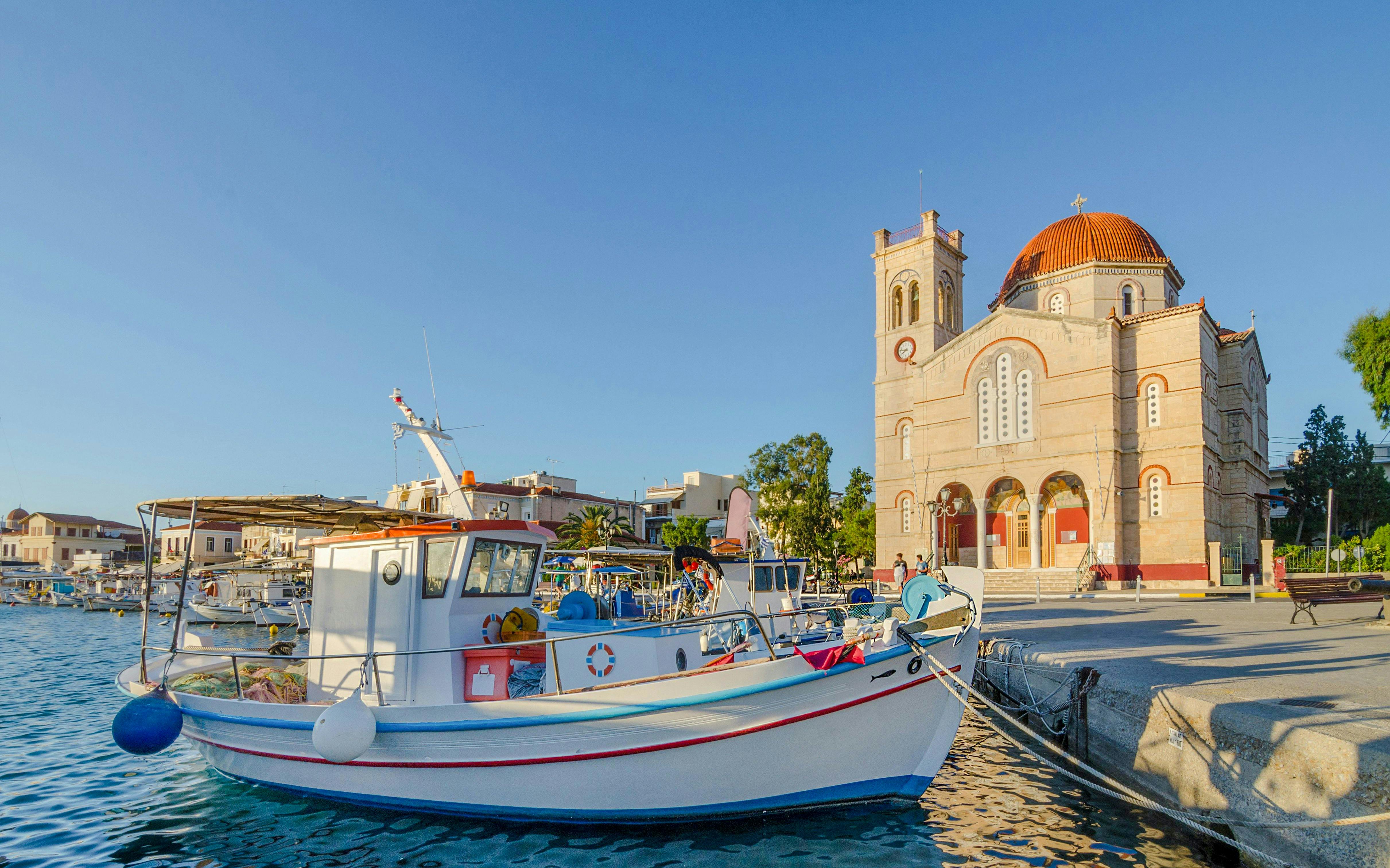Fishing boats docked at Port of Aegina town with a church in the background, Aegina island, Greece.