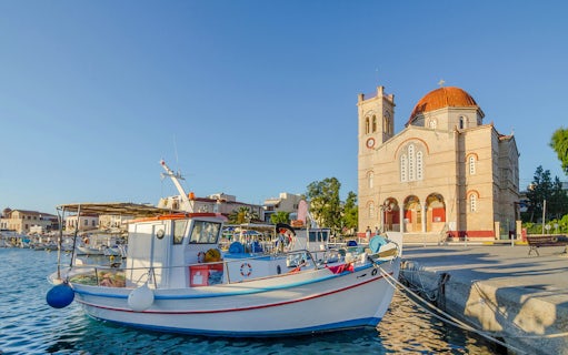 Fishing boats docked at Port of Aegina town with a church in the background, Aegina island, Greece.