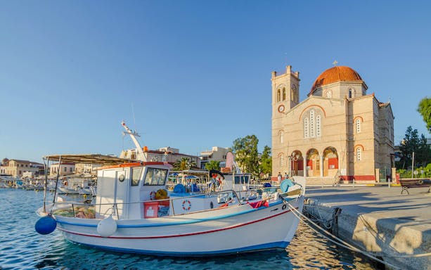 Fishing boats docked at Port of Aegina town with a church in the background, Aegina island, Greece.