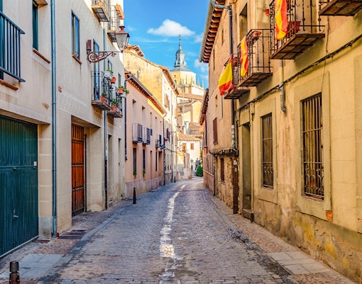 Cobbled medieval street in Segovia with Spanish flags and historic buildings.