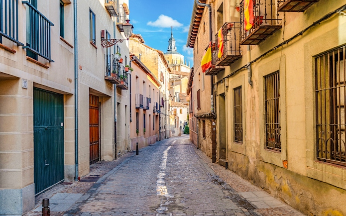 Cobbled medieval street in Segovia with Spanish flags and historic buildings.