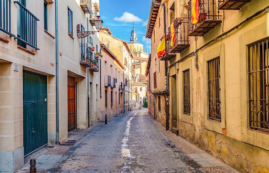 Cobbled medieval street in Segovia with Spanish flags and historic buildings.