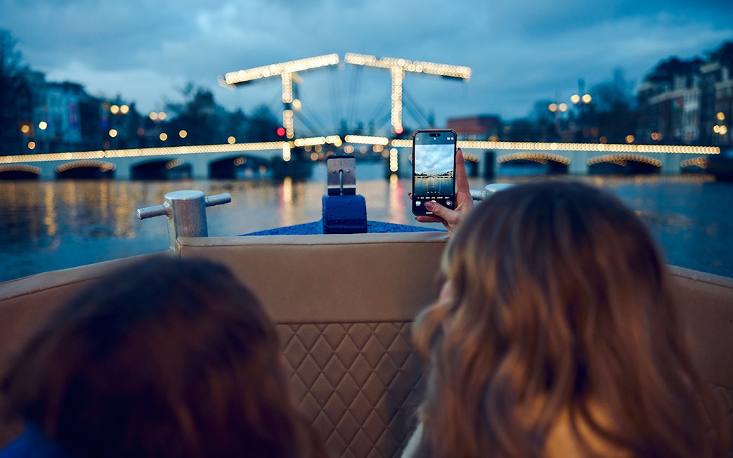 Small group on a boat capturing Amsterdam Light Festival bridge lights.
