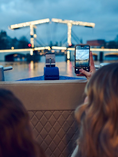 Small group on a boat capturing Amsterdam Light Festival bridge lights.