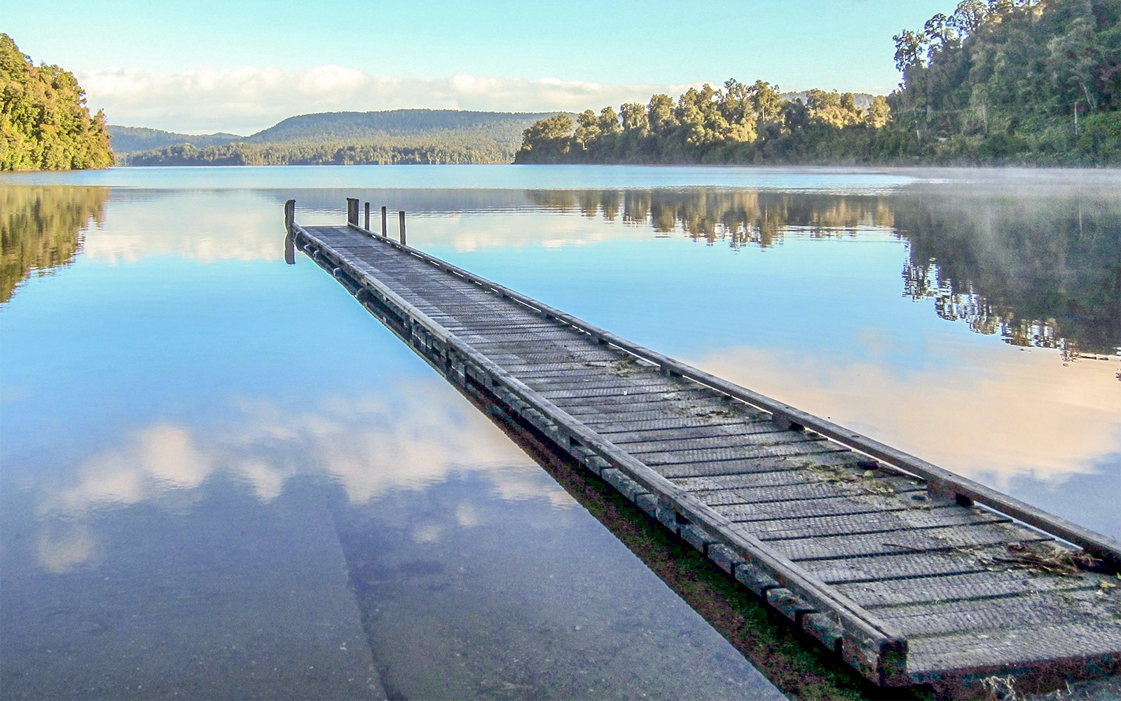 Dock extending into Franz Josef Lake Mapourika with forested hills in the background.