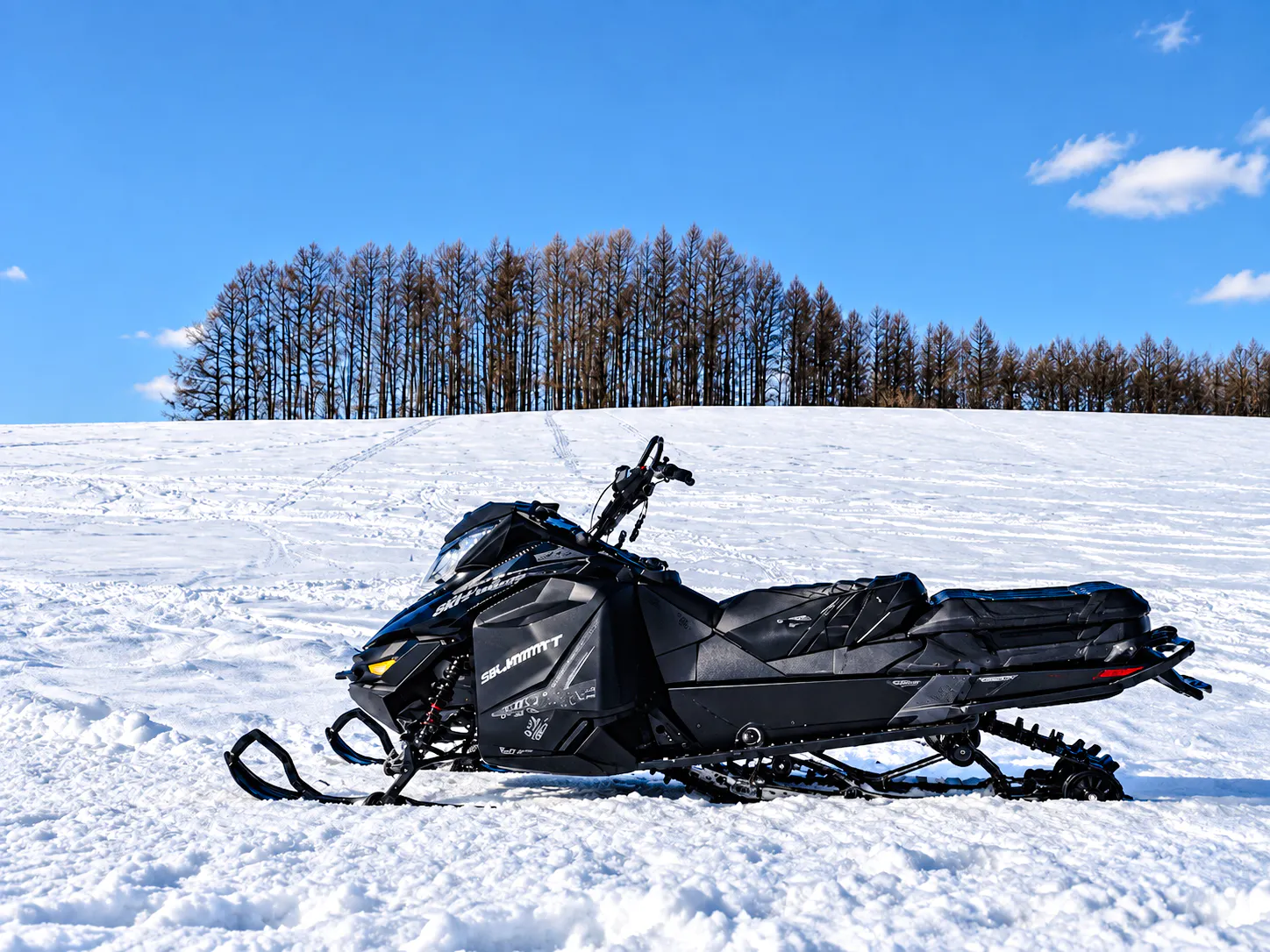 Snowmobile on snowy field at Chiyoda Snow Park, Hokkaido, with trees in the background.