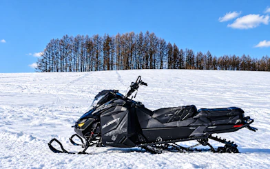 Snowmobile on snowy field at Chiyoda Snow Park, Hokkaido, with trees in the background.