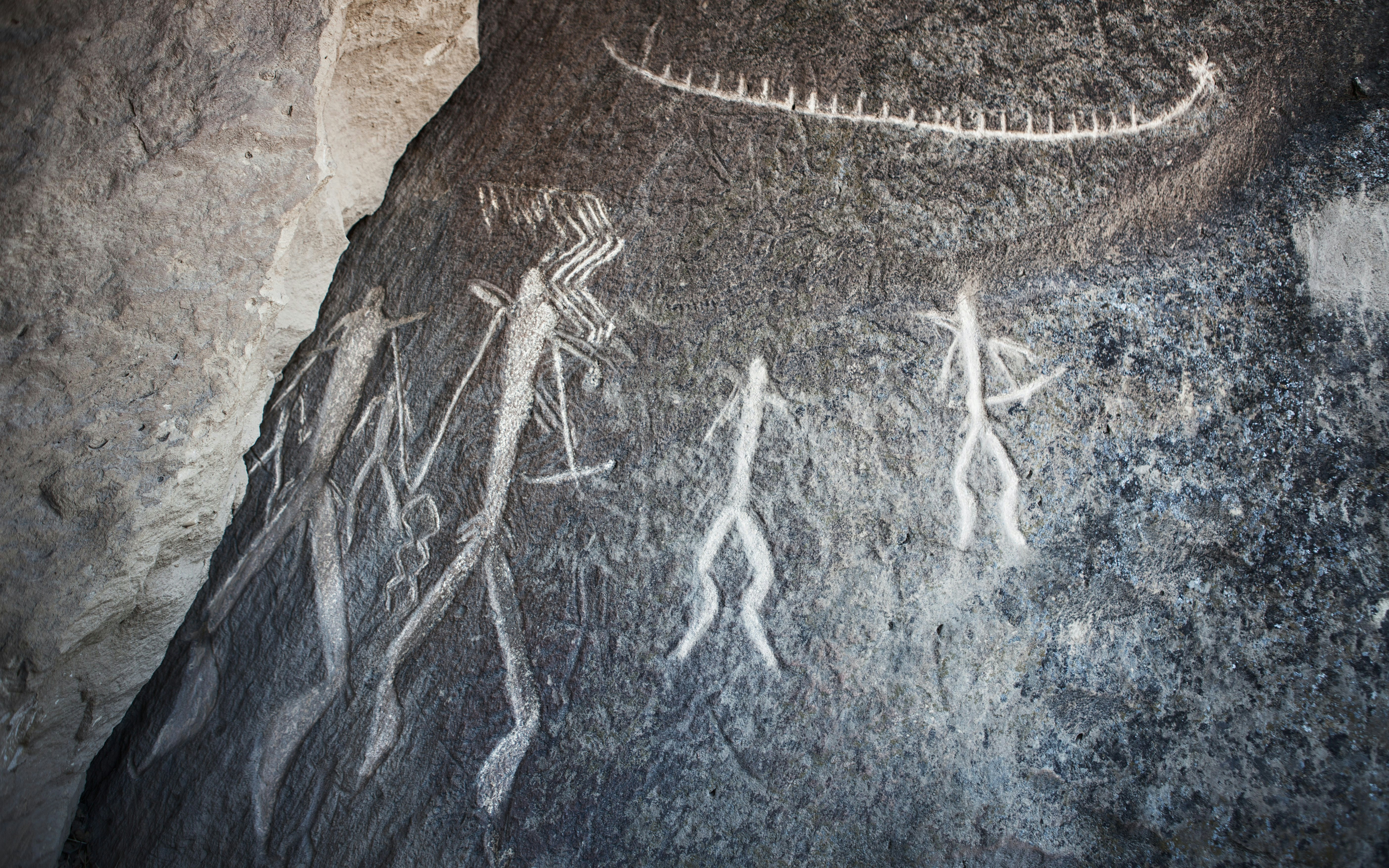 Ancient rock carvings depicting human figures and a serpent on a stone surface.