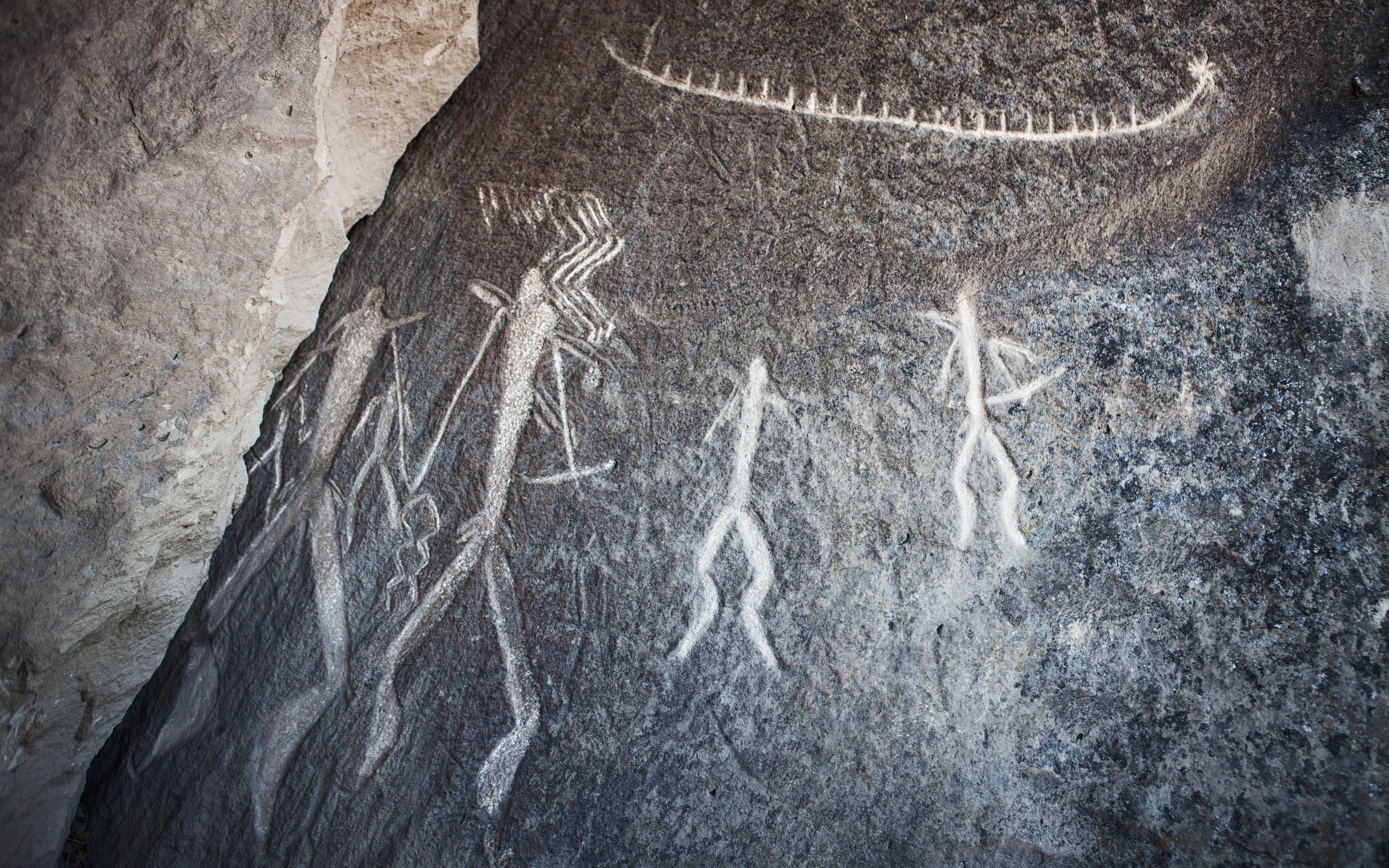 Ancient rock carvings depicting human figures and a serpent on a stone surface.
