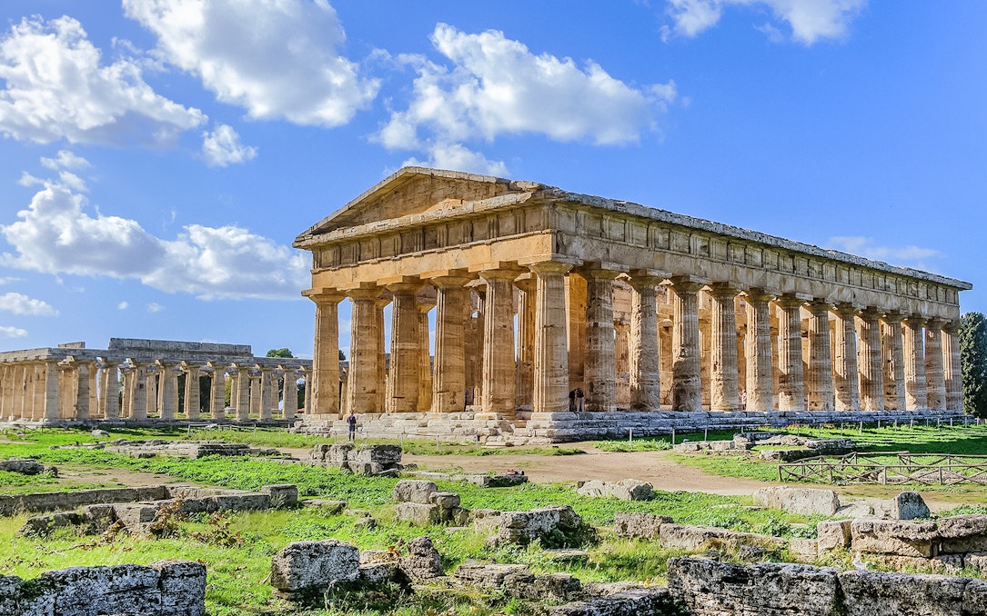 Ancient Greek temple ruins in Paestum, Italy, with clear blue sky.