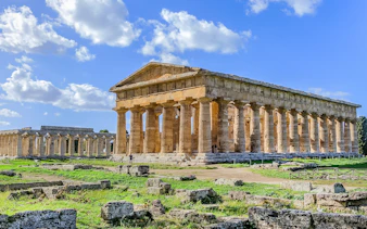 Ancient Greek temple ruins in Paestum, Italy, with clear blue sky.