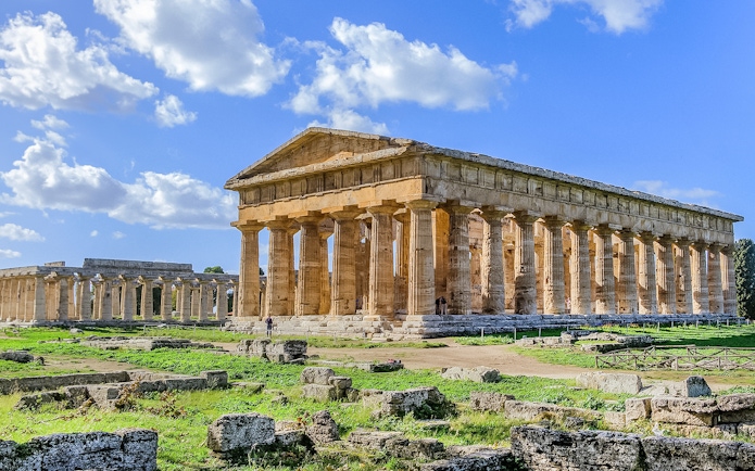 Ancient Greek temple ruins in Paestum, Italy, with clear blue sky.