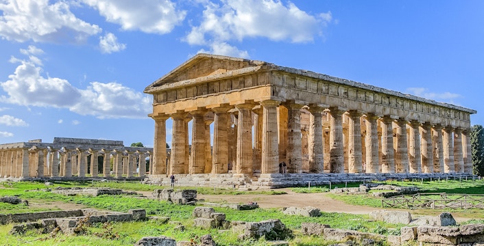 Ancient Greek temple ruins in Paestum, Italy, with clear blue sky.