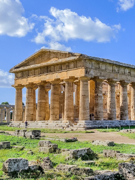Ancient Greek temple ruins in Paestum, Italy, with clear blue sky.