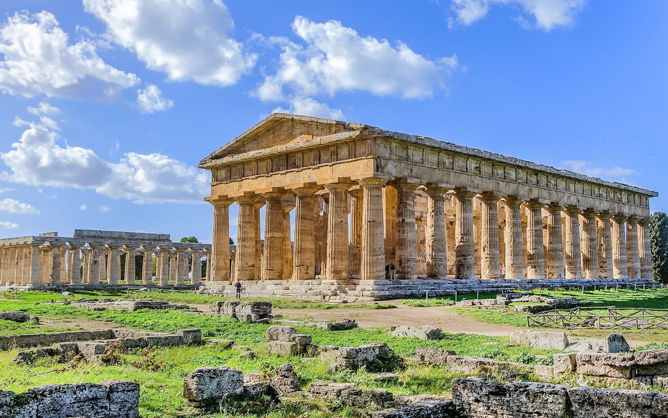 Ancient Greek temple ruins in Paestum, Italy, with clear blue sky.