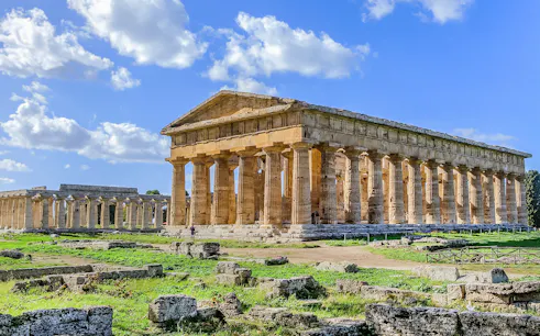Ancient Greek temple ruins in Paestum, Italy, with clear blue sky.