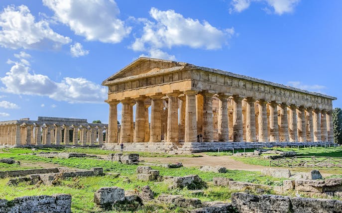 Ancient Greek temple ruins in Paestum, Italy, with clear blue sky.