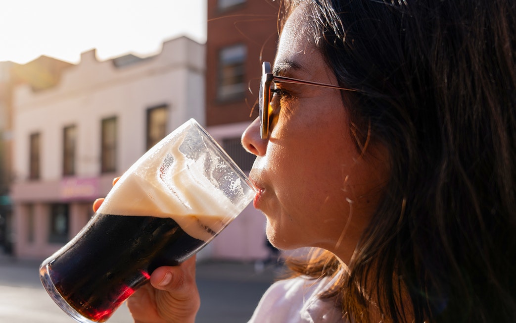 Woman enjoying a pint of dark beer outdoors in a city setting.